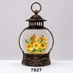 A decorative lantern-shaped glass display with an antique bronze metal frame and base, containing a preserved floral arrangement of yellow sunflowers, green leaves, and orange-and-black butterflies under clear glass. The lantern is centered on a light gray studio background with a white surface, and the number 7827 appears below.