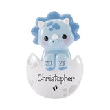 A blue toy dinosaur figurine sitting inside a white egg with the name "Christoph" written on it.