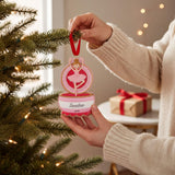 A person is holding a pink ornament with a dancing ballerina figure on a Christmas tree.