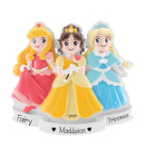 A personalized resin figurine of three princess characters on a white base. The left character has long blonde hair and wears a pink dress, labeled 'Fairly'.