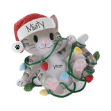 A decorative figurine of a gray tabby kitten wearing a red glitter Santa hat with the name 'Misty' on it, wrapped in green Christmas lights with red, blue, yellow, and green bulbs. The figurine has 'year' printed on its belly and is set against a plain white background.