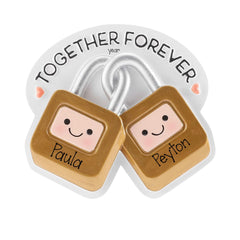 May include: A decorative ornament featuring two interlocking gold-colored padlocks with smiling faces. The left lock is inscribed with the name Paula and the right with Peyton. Above the locks, the text TOGETHER FOREVER is printed with small pink hearts.