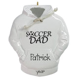 A white ceramic Christmas ornament shaped like a hoodie with a gold hanging loop. The front features the text 'SOCCER DAD' with a soccer ball graphic inside the letter O, and 'Patrick' printed below on the kangaroo pocket area.