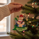 A hand is holding a Christmas ornament that features a smiling fish wearing a red hat and striped shirt, with the name "Michael!" written on it.