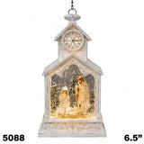 A hanging Christmas clock shaped like a small church or nativity scene, with a distressed white exterior, gold-toned interior lighting, and figurines inside. The top shows a clock face with Roman numerals.