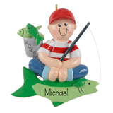 A personalized ornament depicting a smiling boy sitting on a fish, with a fishing rod in his hand. The boy is wearing a red hat and a striped shirt. The ornament has the name "Michael" written on it.