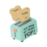 A novelty ceramic toy toaster in mint green with two bread slices popping out. One slice is labeled 'Mark' and the other 'Maddie years'.