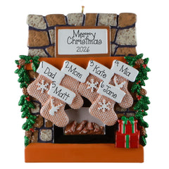 A Christmas ornament with a fireplace and stockings. The stockings are personalized with names and snowflakes, and there is a sign above the fireplace that reads "Merry Christmas 2026".